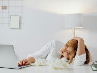 Tired woman resting head on desk with laptop, showing workplace exhaustion.